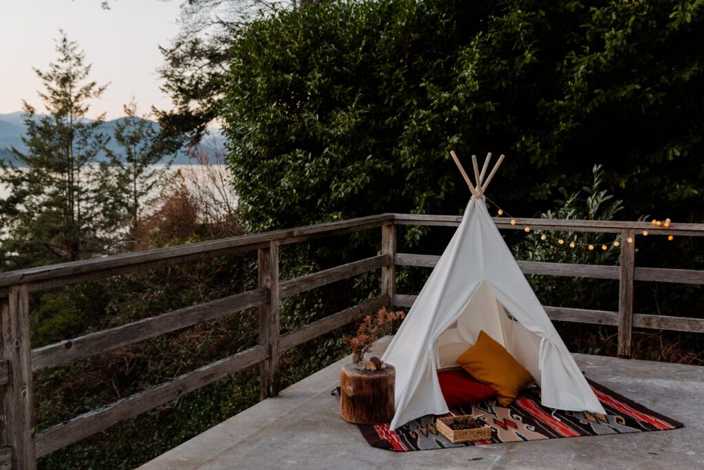 3932976-3932976 Boho styled tent with rug and pillows located on terrace with wooden fence with picturesque view to sea forest and mountains